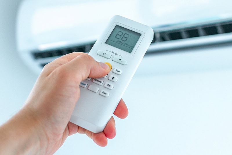 How Much Does it Cost to Install a Ductless Mini Split? Photo of someone adjusting heating or cooling with a remote.